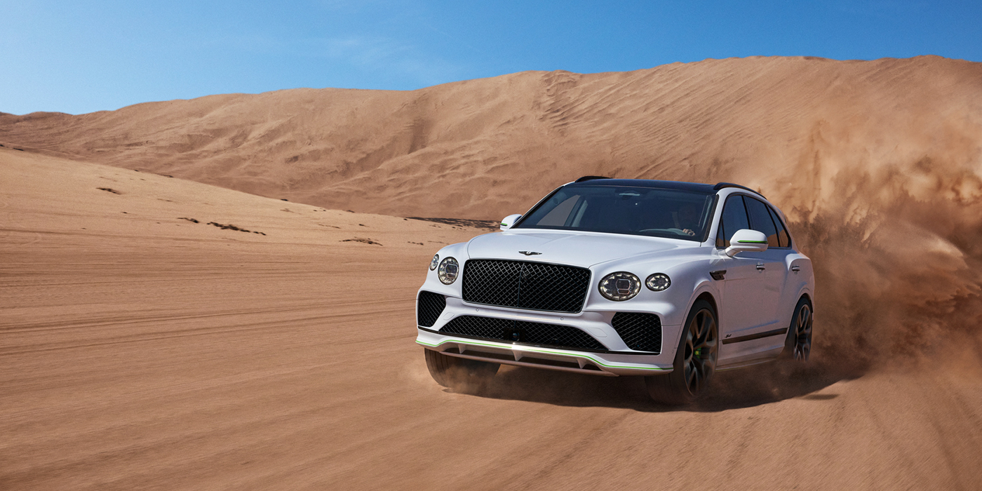 Bentley Birmingham Bentley Bentayga Speed SUV front three quarter in Snow Quarts Pearlescent by Mulliner white paint driving dynamically through the desert