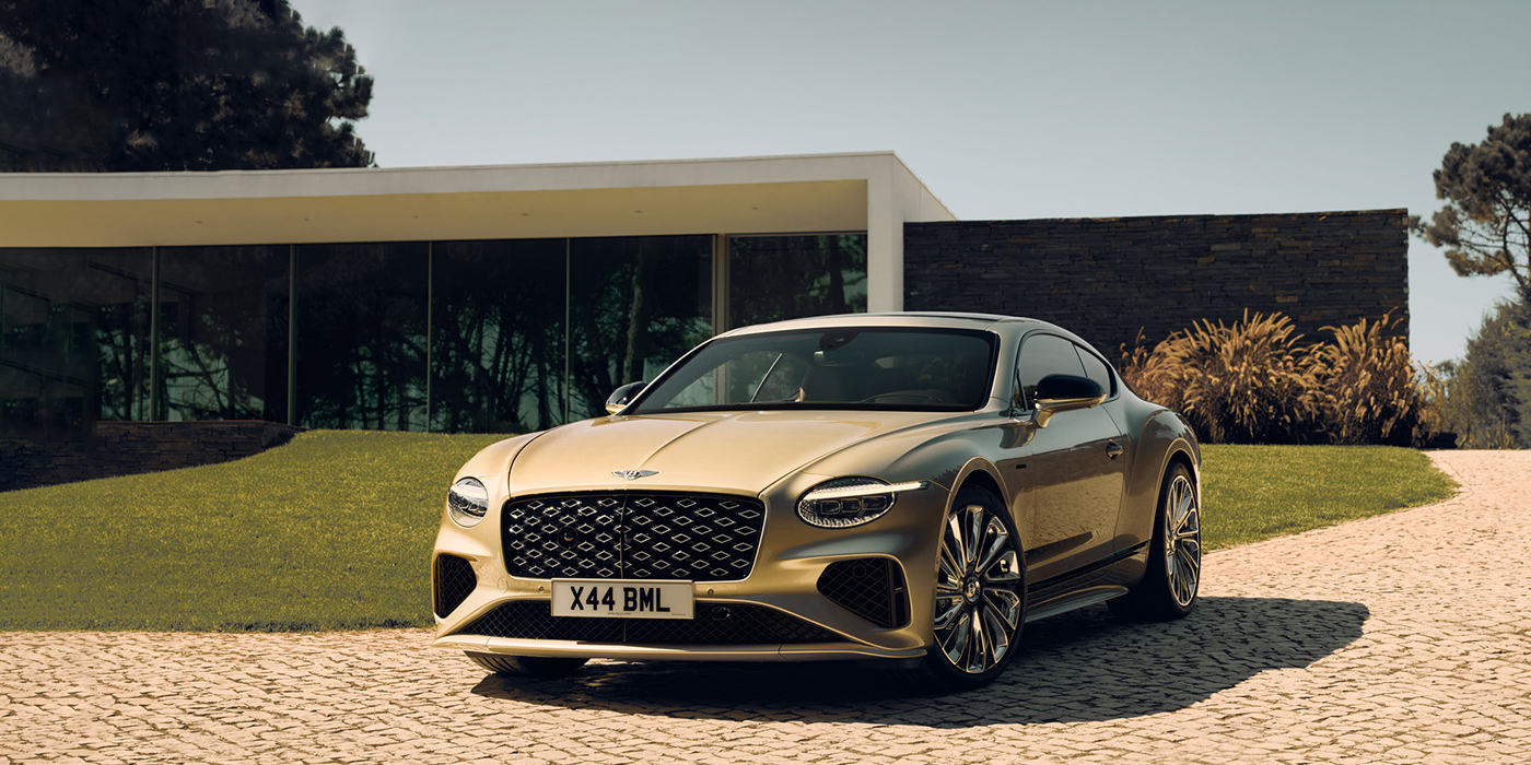 Bentley Birmingham Bentley Continental GT Mulliner coupe front three quarters in Patina paint parked outside a glass fronted building with a grass lawn behind it