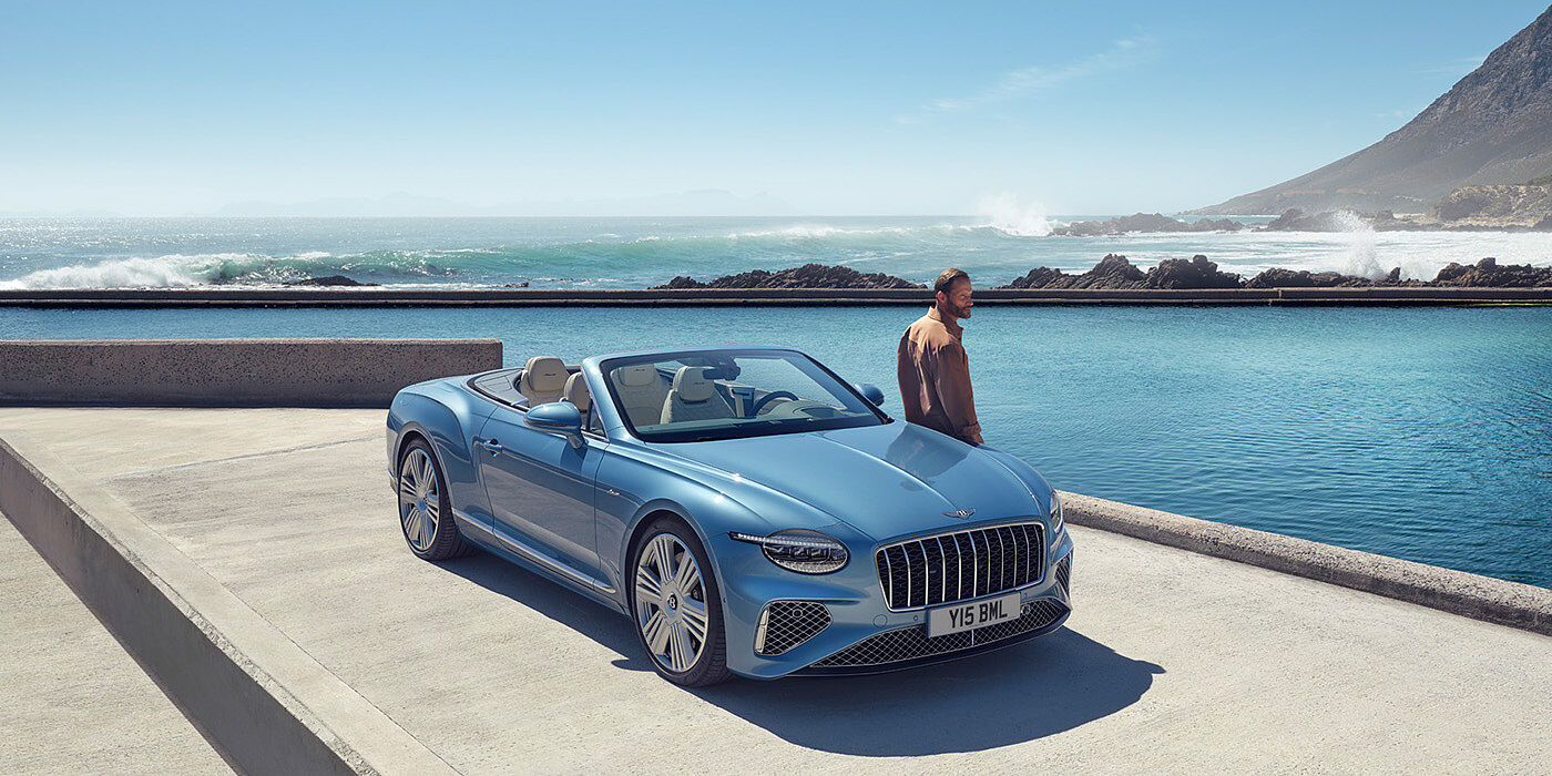 Bentley Birmingham New Bentley Continental GTC Azure convertible front view in Light Windsor blue paint with 22 inch ten spoke wheels parked by the sea in the sunshine