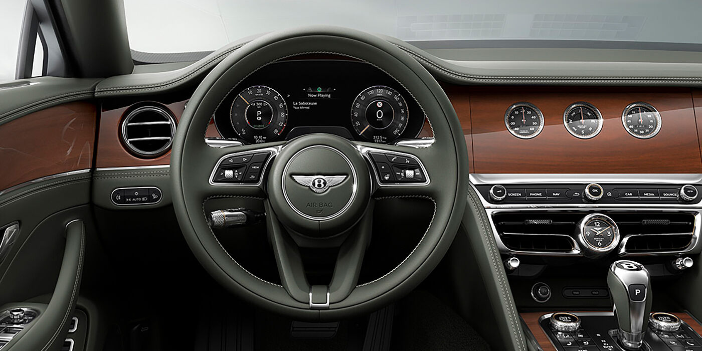 Bentley Birmingham New Bentley Flying Spur sedan front cabin in Cumbrian Green hide and Crown Cut walnut veneer showing steering wheel and Rotating Display with three clocks on face