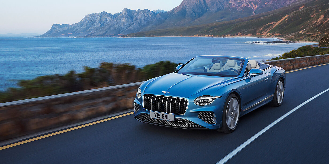 Bentley Birmingham New Bentley Continental GTC Azure convertible in Light Windsor blue paint with 22 inch Azure wheels and chrome grill, driving dynamically by the sea