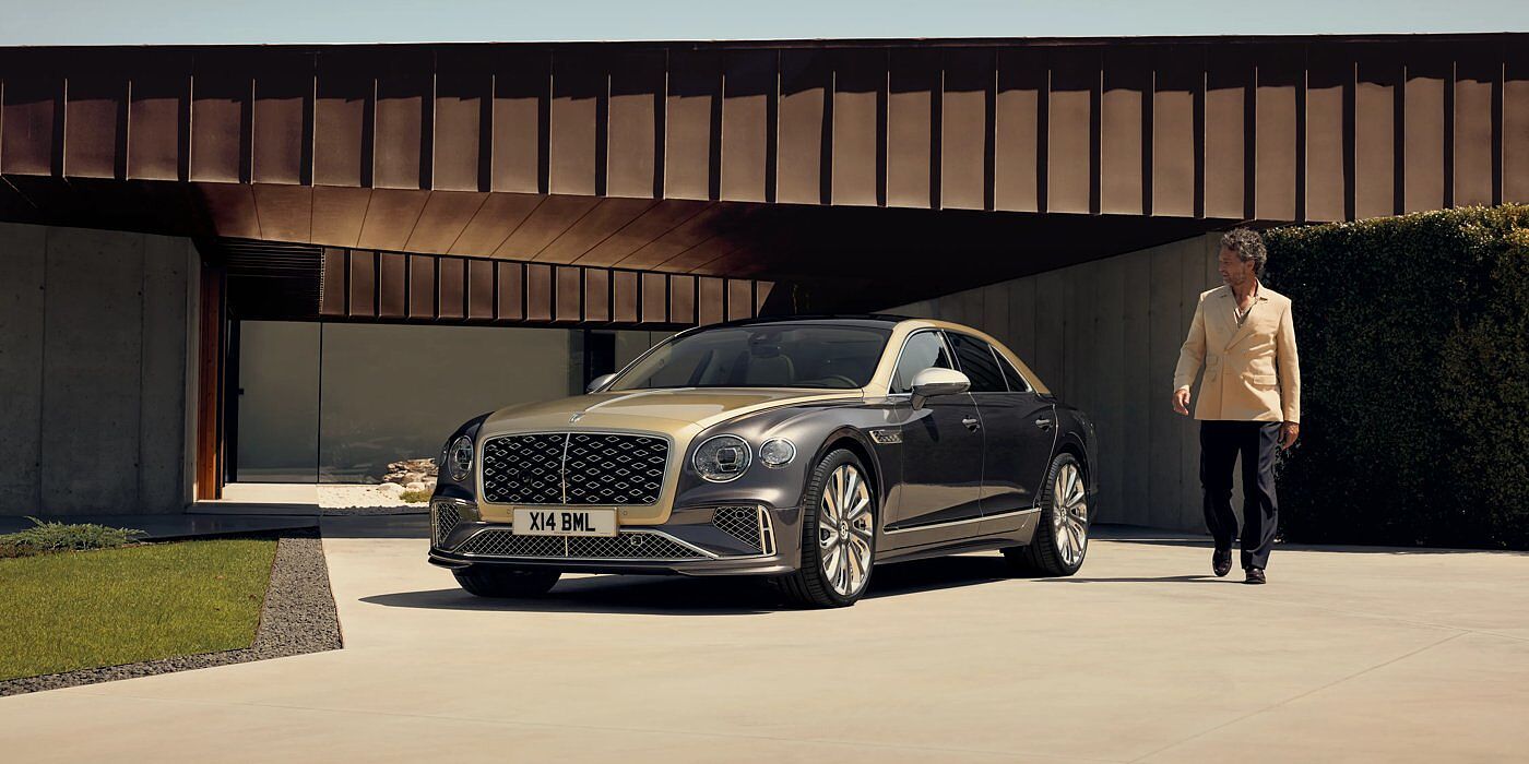 Bentley Birmingham Bentley New Flying Spur Mulliner V8 hybrid sedan front three quarters in Rose Gold over Magnetic paint, parked near modern home