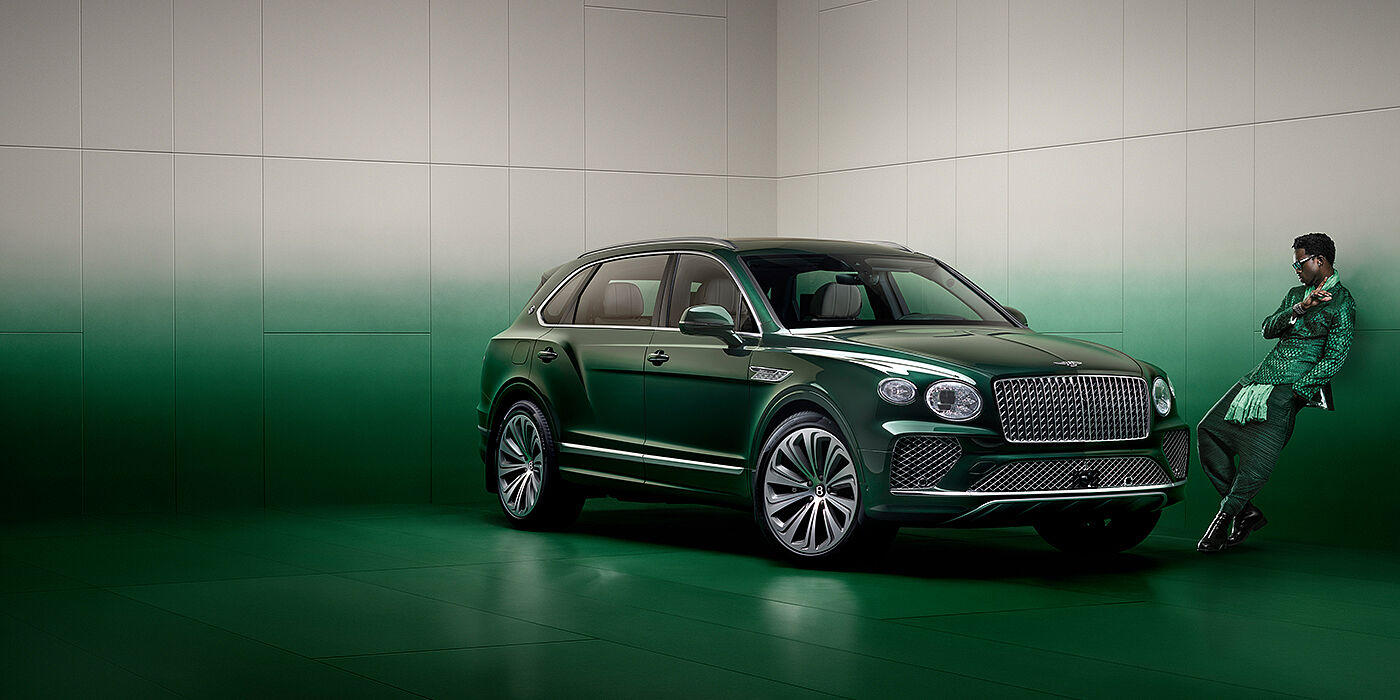 Bentley Birmingham Wisdom K leans against wall next to Bentley Bentayga Extended Wheelbase Atelier Edition SUV in Light Emerald green paint