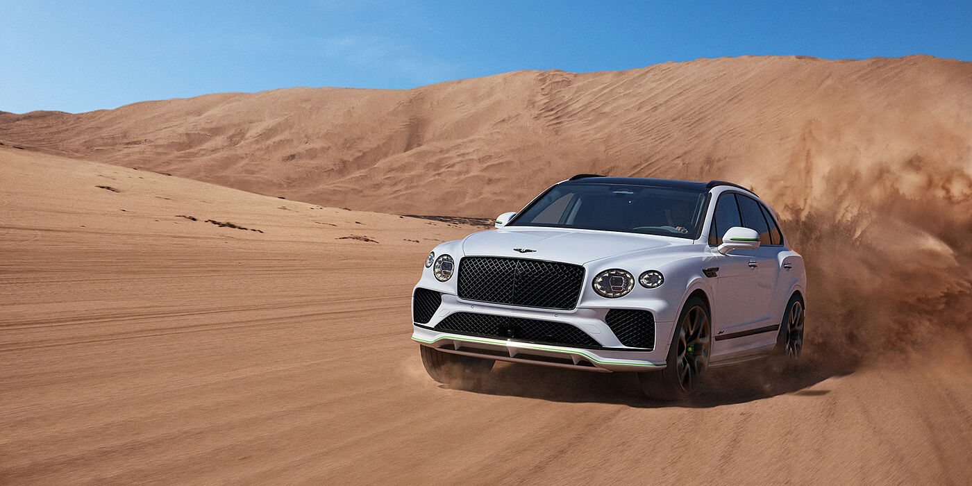 Bentley Birmingham Bentley Bentayga Speed SUV front three quarter in Snow Quarts Pearlescent by Mulliner white paint driving dynamically through the desert