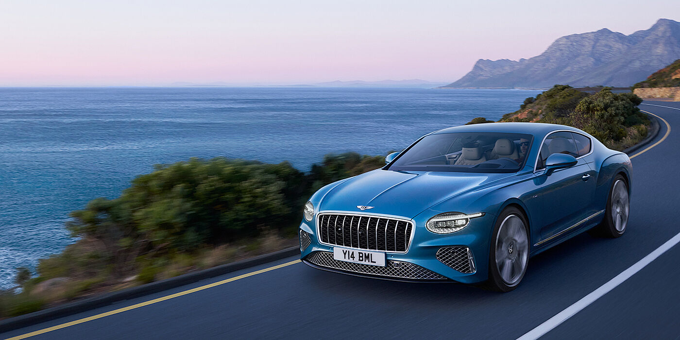 Bentley Birmingham New Bentley Continental GT Azure coupe in Light Windsor blue paint with 22 inch Azure wheels and chrome grill, driving dynamically by the sea