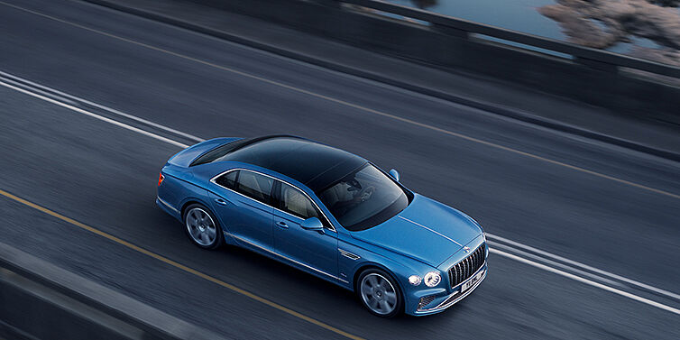 Bentley Birmingham New Bentley Flying Spur Azure sedan in Light windsor blue paint by Mulliner, with 22 inch Azure wheels seen from overhead driving dynamically on a country road