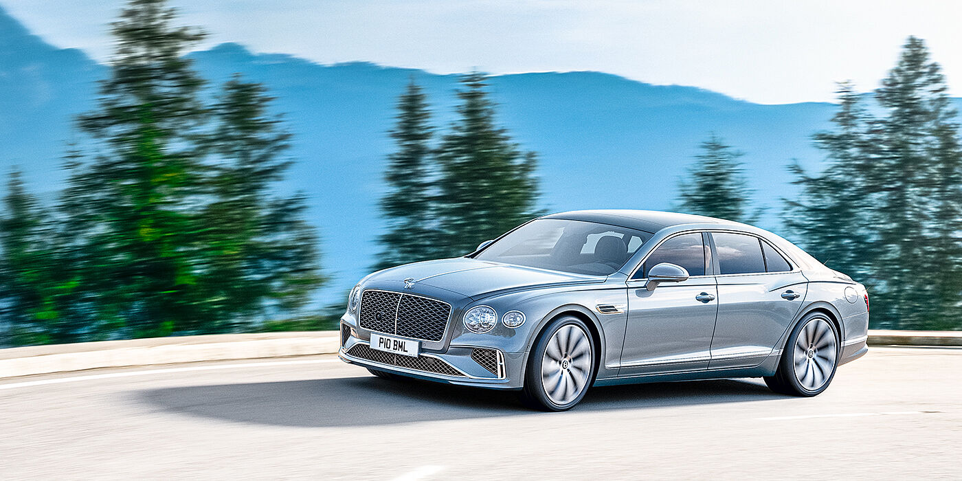 Bentley Birmingham New Bentley Flying Spur sedan side view in Silverlake paint with ten spoke wheels and chrome matrix grille driving dynamically on a mountain road