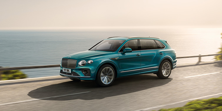 Bentley Birmingham Bentley Bentayga Extended Wheelbase Azure SUV in Topaz blue paint driving dynamically by the ocean