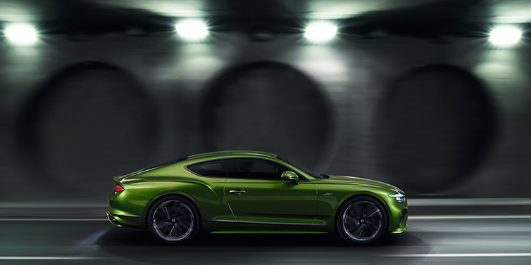 Bentley Birmingham Bentley Continental GT Speed coupe profile in Tourmaline Green driving dynamically past a concrete wall at night