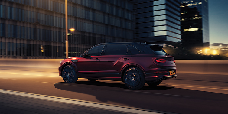 Bentley Birmingham Bentley Bentayga Extended Wheelbase Mulliner SUV in Cricket Ball red paint driving dynamically in city at night