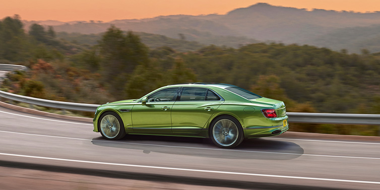 Bentley Birmingham Bentley Flying Spur Speed sedan side profile in Tourmaline Green paint driving dynamically on a mountain road at sunset