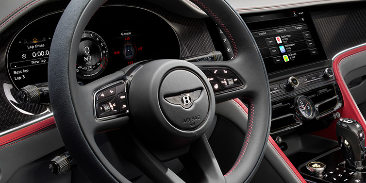 Bentley Birmingham Bentley Flying Spur Speed sedan front interior detail showing steering wheel and driver screens surrounded with Hotspur red and Gravity Grey hides